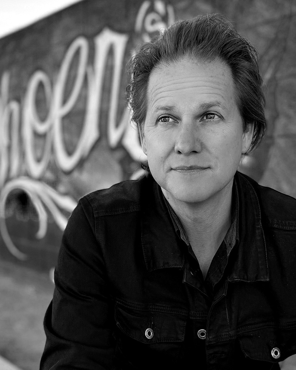 Jeremy Veatch in a dark denim jacket in front of a painted Phoenix mural, looking past the camera
