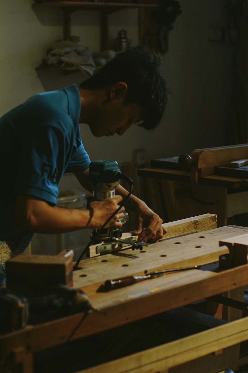 Carpenter guiding a router across a board at his workshop bench